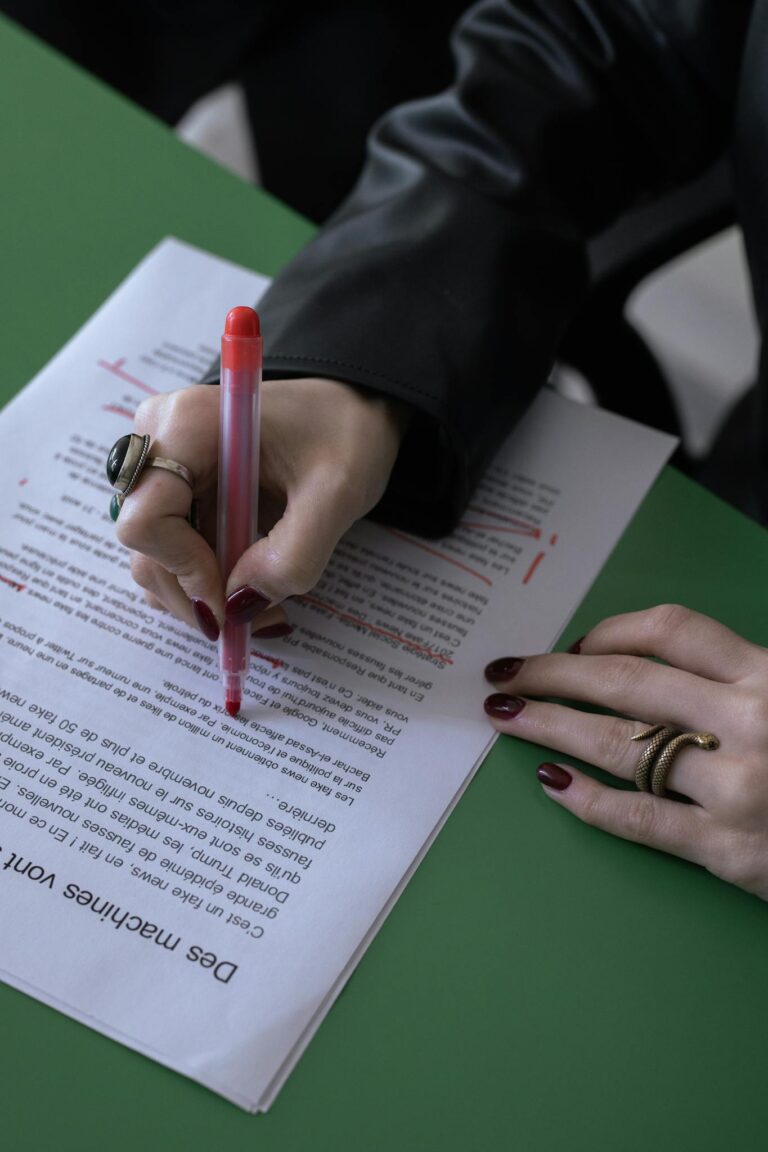 A person edits a document with a red pen on a green table, highlighting corrections.